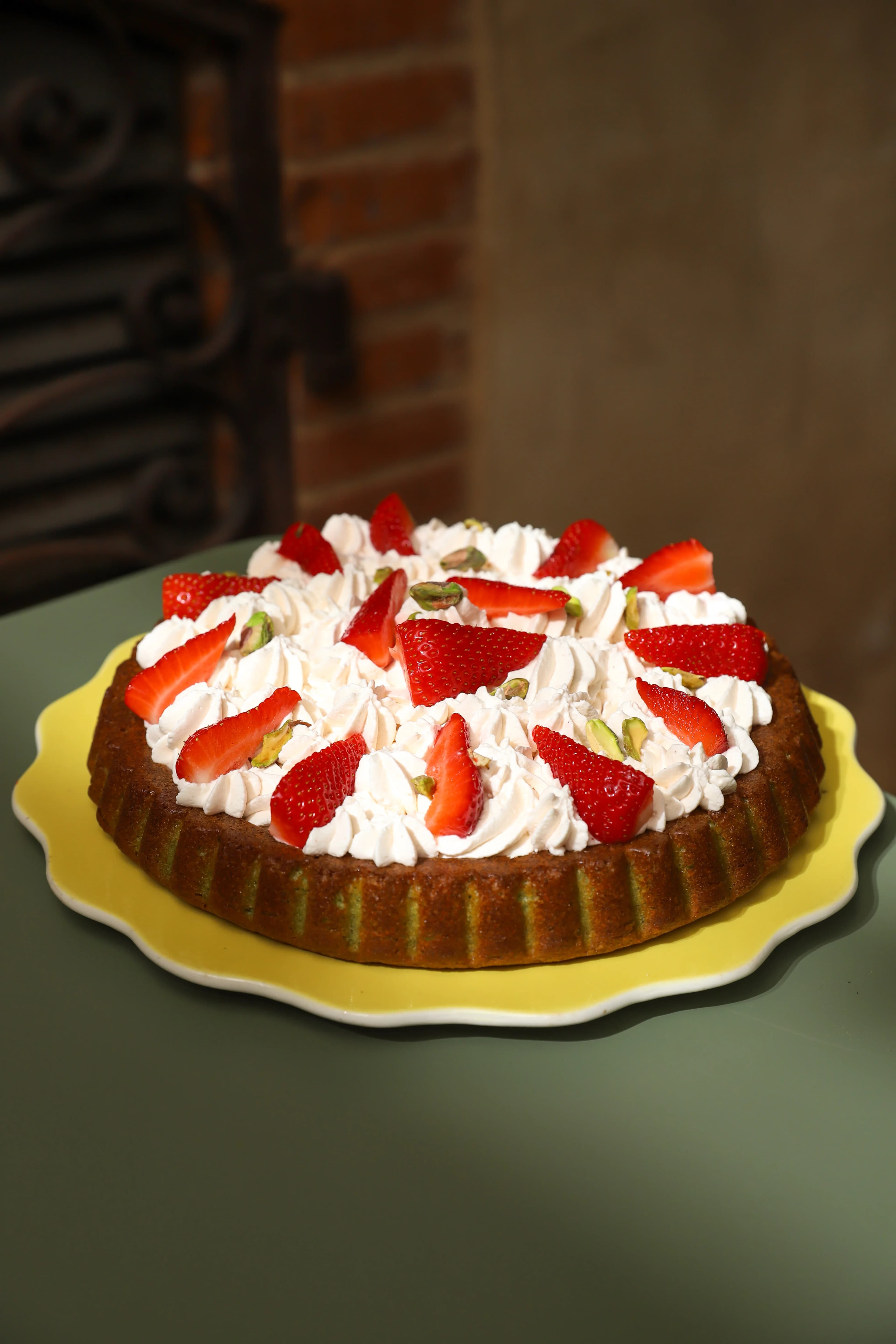 Un gâteau entier maison du Jardin de Pauline, garni de fraises, de crème et de pistaches